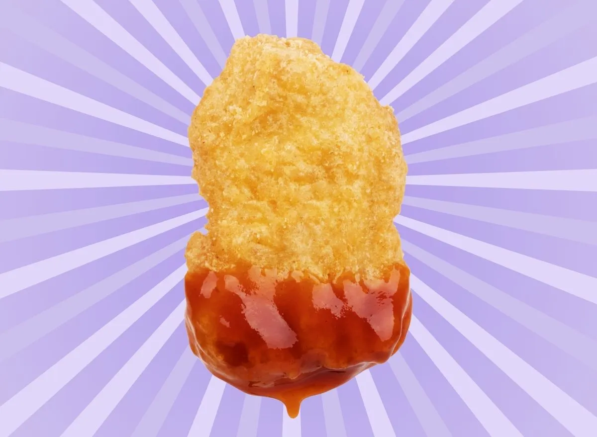 A single chicken nugget dipped in ketchup set against a colorful background