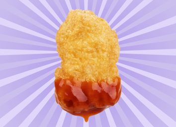 A single chicken nugget dipped in ketchup set against a colorful background