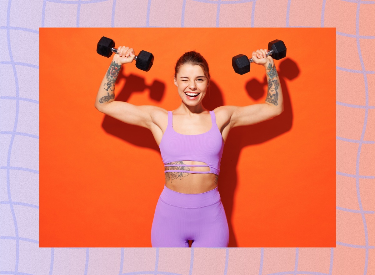 fit woman wearing purple sports bra and leggings doing dumbbell shoulder press in front of orange backdrop