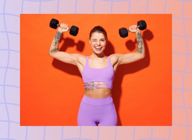 fit woman wearing purple sports bra and leggings doing dumbbell shoulder press in front of orange backdrop