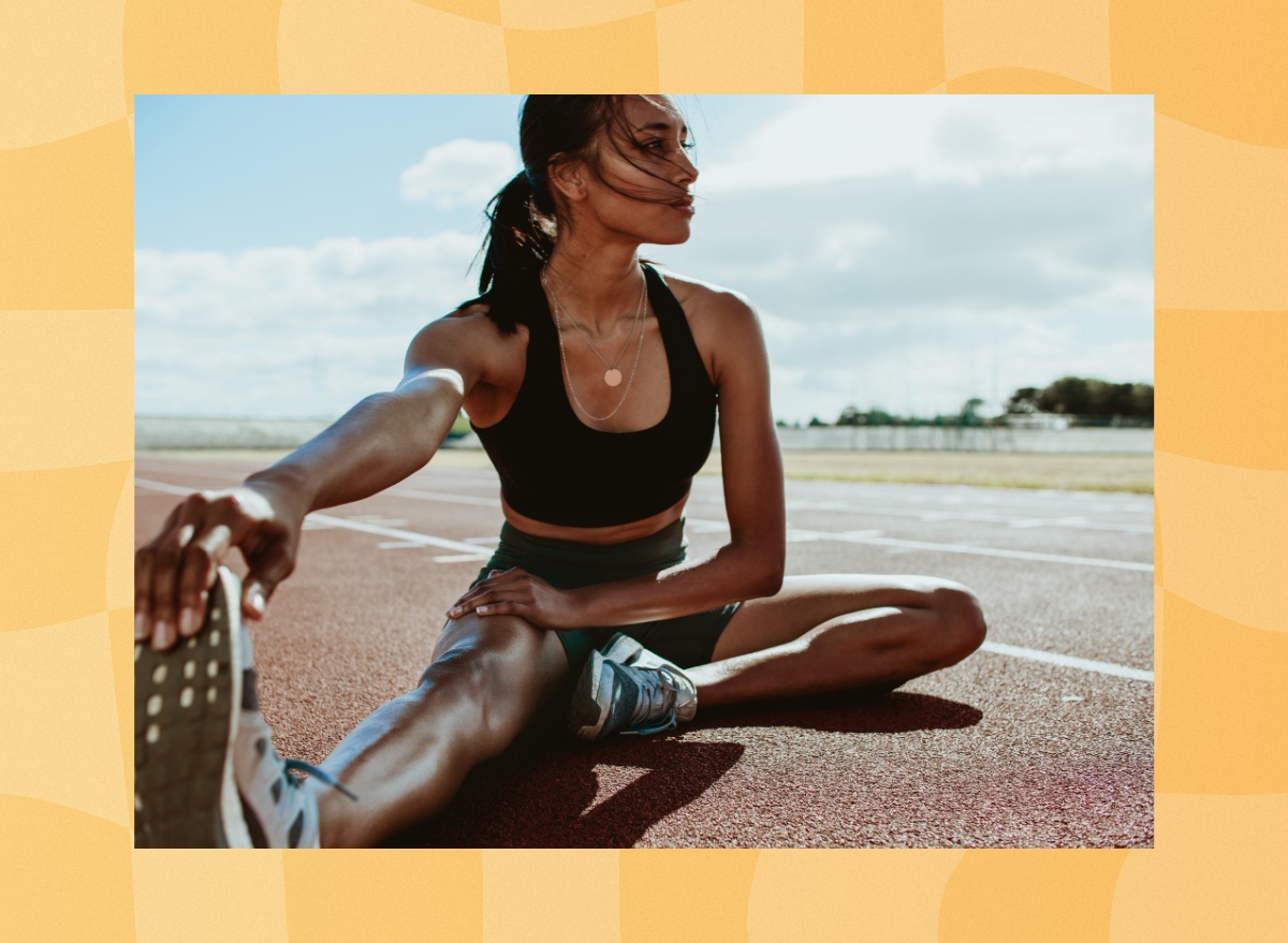 fit brunette woman stretching outdoors on track before running workout on sunny day