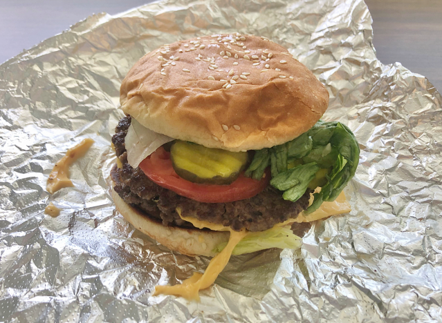 a cheeseburger with tomatoes and pickles on a crinkled sheet of tinfoil.