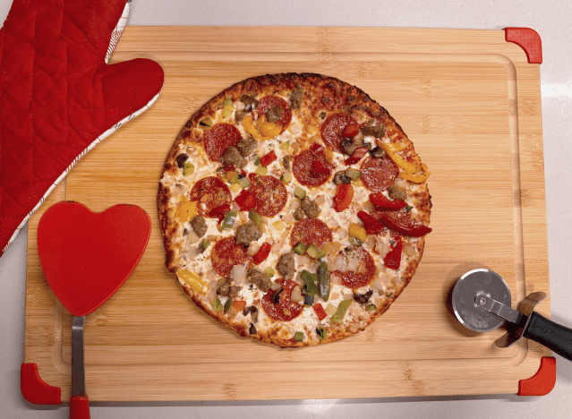 a cauliflower pizza on a cutting board with a red oven mitt and a pizza cutter.