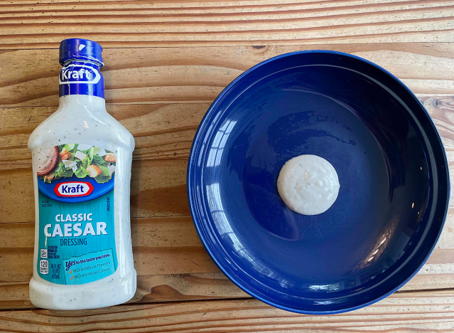 a bottle of caesar dressing next to a blue plate with dressing on it. 