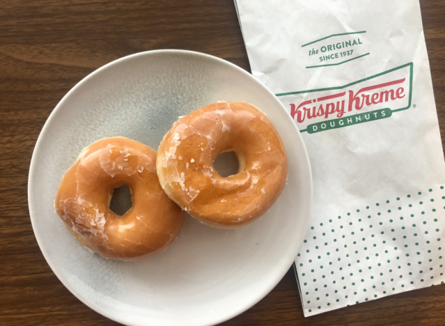 two glazed donuts from krispy kreme on a plate with a bag.