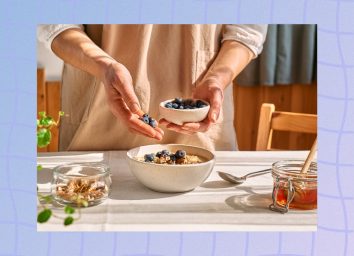 close-up of woman's hands adding blueberries to oatmeal breakfast in bright kitchen
