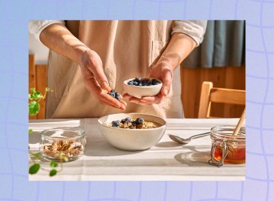 close-up of woman's hands adding blueberries to oatmeal breakfast in bright kitchen