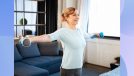 mature, happy woman lifting dumbbells while exercising in her living room