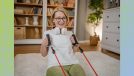 happy older woman with glasses doing resistance band floor exercise in living room
