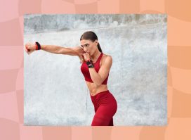 focused, fit, and muscular woman in red athletic set throwing boxing punches outside in front of cement wall