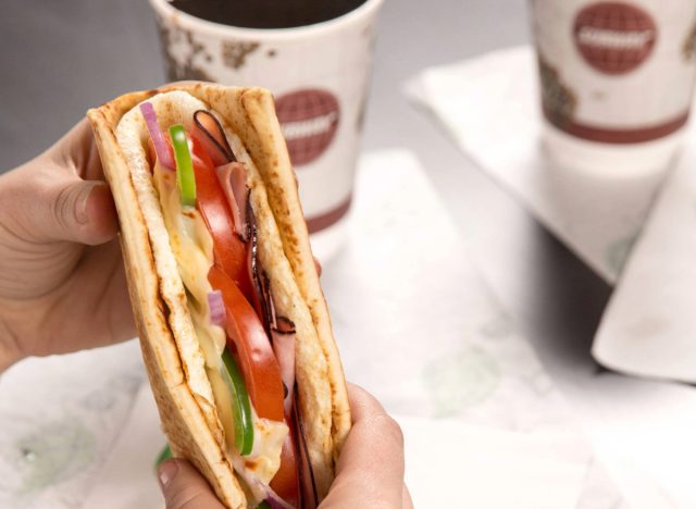 person holding subway's breakfast flatbread next to a cup of coffee