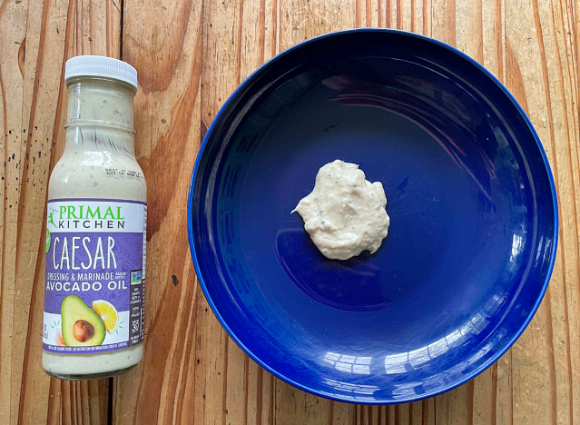 a bottle of caesar dressing next to a blue plate with a blob of dressing on it. 