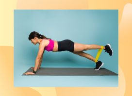 fit brunette woman in pink sports bra and black shorts doing resistance band plank leg lifts