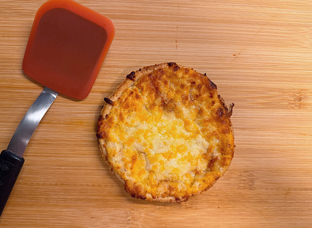 a mini cheese pizza on a cutting board with a red spatula. 