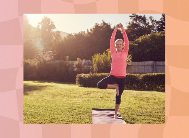 senior woman in pink long-sleeve top and black leggings doing balancing exercise or tree pose on yoga mat in sunny backyard