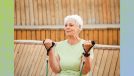 senior woman in green t-shirt doing resistance band bicep curls in front of fence outdoors