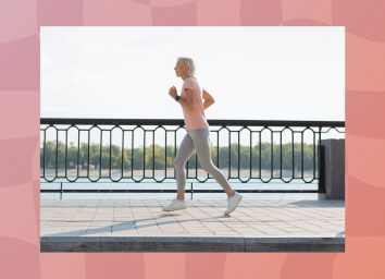fit senior woman in pink t-shirt and gray leggings running along the waterfront on sunny day