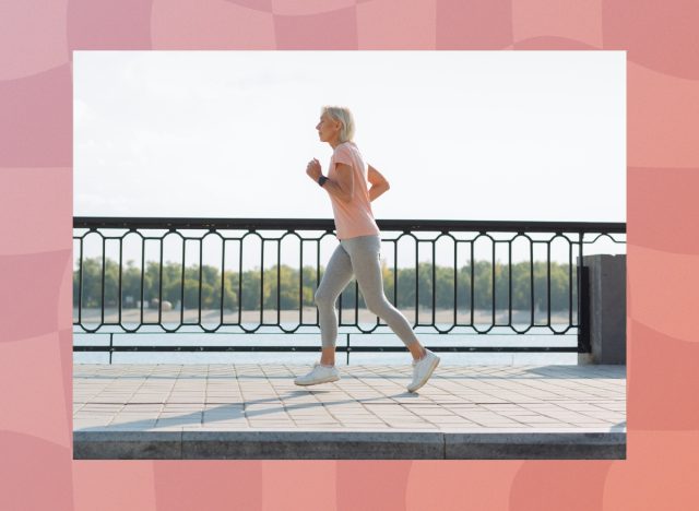 fit senior woman in pink t-shirt and gray leggings running along the waterfront on sunny day