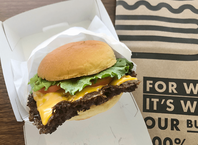 a cheeseburger with lettuce and tomatoes in a takeout box. 