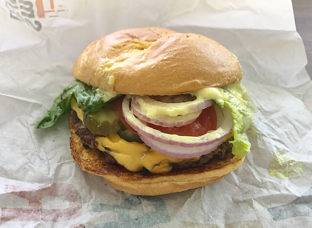 a cheeseburger with pickles, onions and tomatoes on a paper.