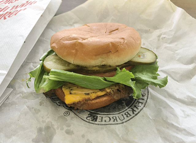 a cheeseburger with lettuce, pickles, tomatoes on a paper. 