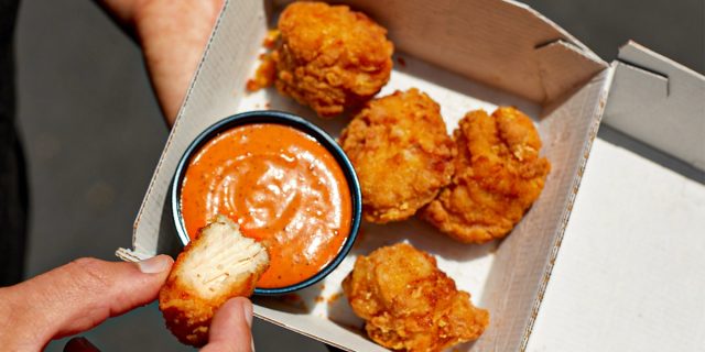 person dipping taco bell's crispy chicken nugget into bell sauce
