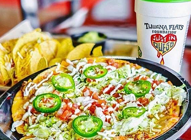 tijuana flats mexican pizza with a side of chips and a drink.