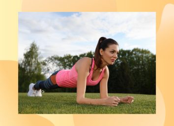 fit brunette woman wearing pink tank, leggings, and white sneakers doing forearm plank exercise in park