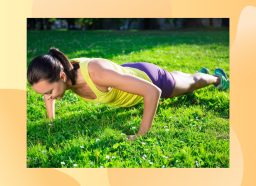 brunette woman in yellow tank and purple shorts doing pushups in bright grassy lawn