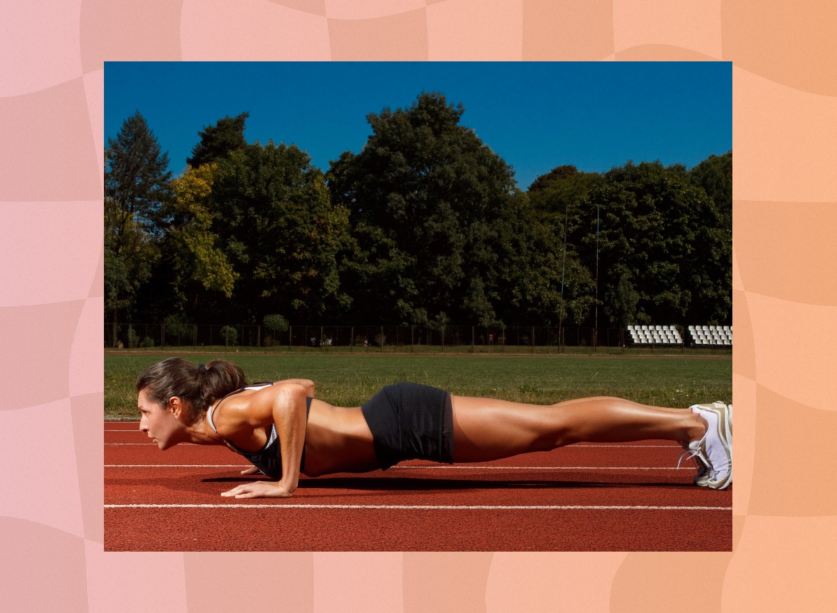 fit woman in black sports bra and shorts doing pushups outdoors on a track