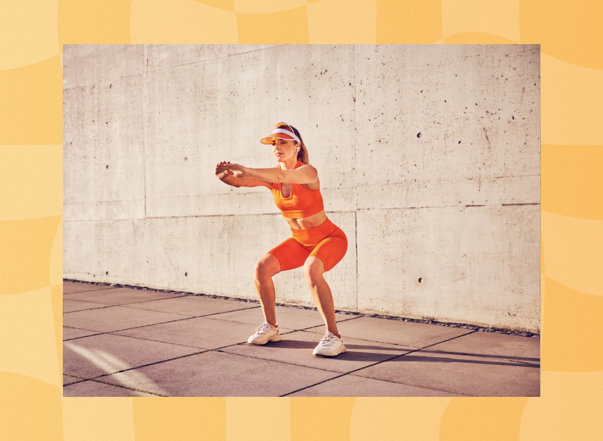 fit woman in orange biker shorts and sports bra doing bodyweight squat exercise outdoors on court