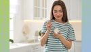 happy woman in green and white striped shirt eating greek yogurt out of small jar in bright white kitchen