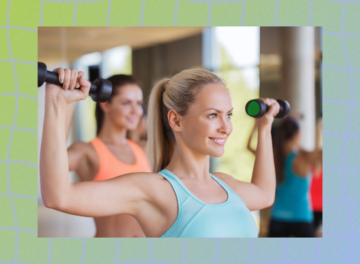 happy blonde woman wearing blue sports tank lifting weights in a bright workout class