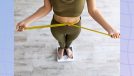 close-up of woman in green athletic set measuring waistline and standing on scale