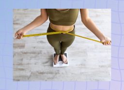 close-up of woman in green athletic set measuring waistline and standing on scale