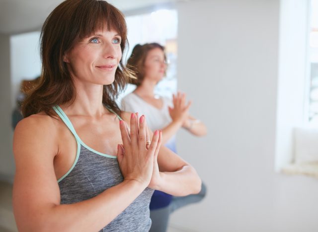 fit mature woman doing prayer pose in yoga class