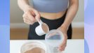 close-up of woman's hands scooping protein powder into a cup to make a smoothie
