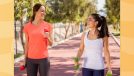 two happy women doing walking workout outdoors on track while holding dumbbells