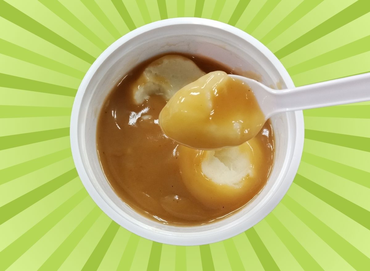 A spoonful of fast-food mashed potatoes from a white cup set against a colorful green background