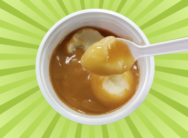 A spoonful of fast-food mashed potatoes from a white cup set against a colorful green background