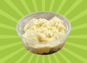A closeup of store-bought potato salad in a plastic container set against a vibrant green background