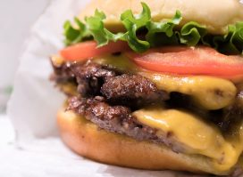 A closeup of the double cheeseburger with tomato lettuce and onion, from Shake Shack.