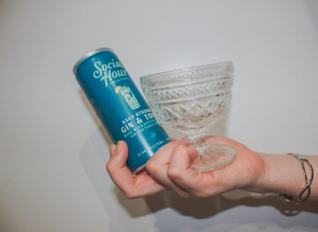 hand holding a glass and canned cocktail on a white background