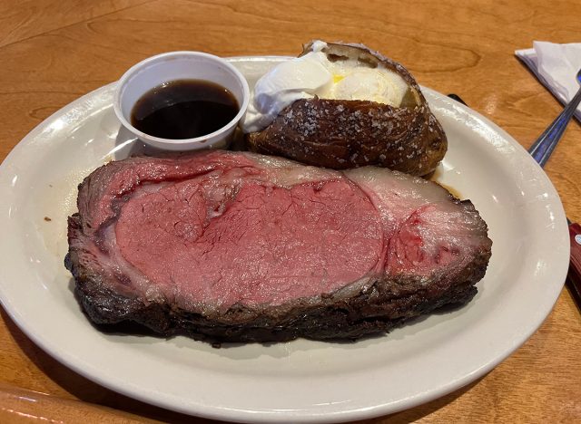 Prime rib with au jus and baked potato on a white plate at Texas Roadhouse