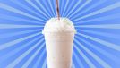 A classic vanilla milkshake in a see-through plastic cup with a straw set against a vibrant blue background