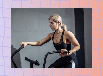 blonde woman at the gym using the air bike in front of gray cement wall