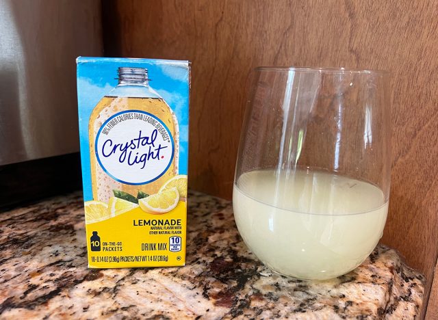 A container of Crystal Light brand lemonade packets next to a small glass of the beverage.
