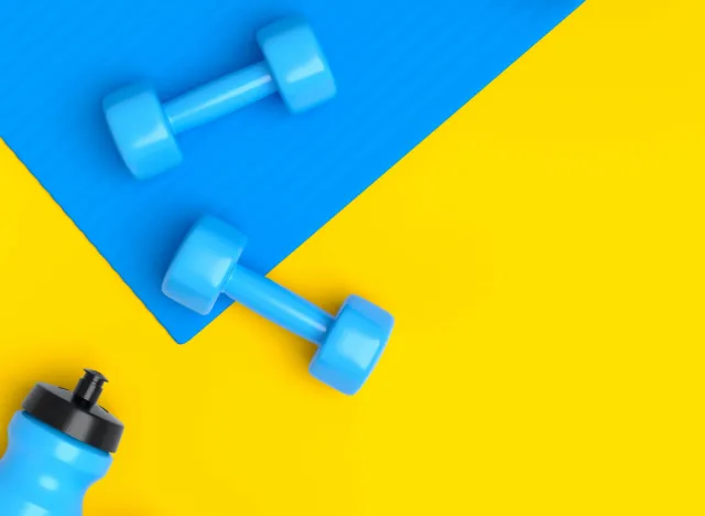 blue dumbbells on blue yoga mat next to blue water bottle, fitness concept