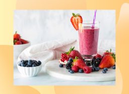 fresh fruit smoothie in tall glass surrounded by fresh berries on white countertop