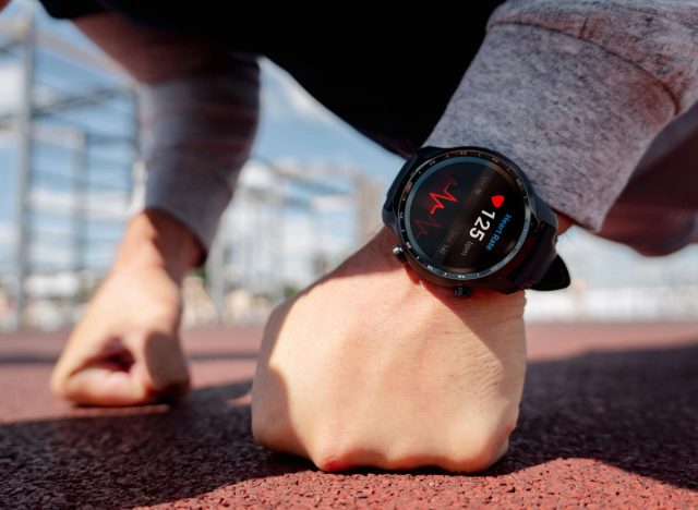 close-up of man's watch and heart rate displayed on screen as he does pushups outdoors on track